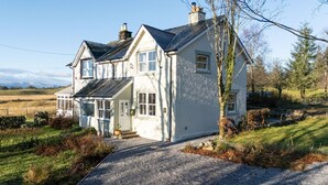 A two-story house with a front porch, a stone wall, and a gravel driveway. - Craignair -  a house that sleeps 4 guests  in 2 bedrooms (Castle Douglas)
