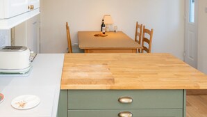 A kitchen with a wooden countertop, a green cabinet with two drawers, a toaster, and a dining table with chairs. - Craignair - a house that sleeps 4 guests in 2 bedrooms (Castle Douglas)