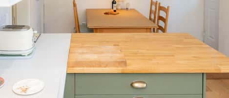 A kitchen with a wooden countertop, a green cabinet with two drawers, a toaster, and a dining table with chairs.