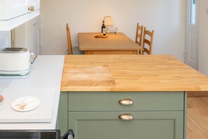 Une cuisine avec un plan de travail en bois, un meuble vert avec deux tiroirs, un grille-pain et une table à manger avec des chaises.