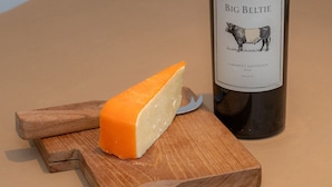 A wedge of cheese on a wooden cutting board with a bottle of Big Belt Cabernet Sauvignon 2024 beside it. - Craignair - a house that sleeps 4 guests in 2 bedrooms (Castle Douglas)