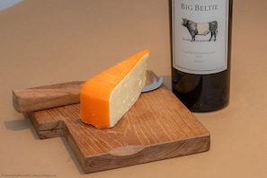 A wedge of cheese on a wooden cutting board with a bottle of Big Belt Cabernet Sauvignon 2024 beside it. - Craignair -  a house that sleeps 4 guests  in 2 bedrooms (Castle Douglas)
