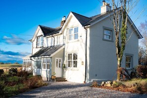 Une maison à deux étages, avec une façade blanche, un porche à l’avant et une allée gravillonnée.