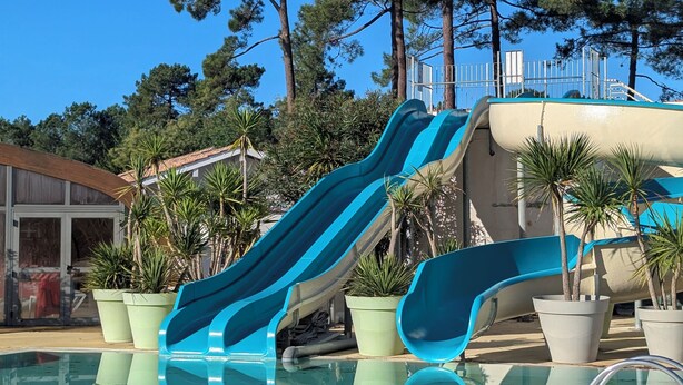 Un espace piscine avec deux toboggans bleus et un ciel dégagé.