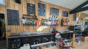 Un espace bar aux murs en bois, agrémenté de plusieurs tableaux noirs où sont affichés les menus des boissons et des plats, ainsi que de diverses bouteilles et verres disposés sur des étagères.