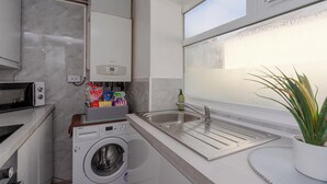 Cocina compacta con lavadora, microondas, lavaplatos y ventana con vistas.