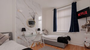Un dormitorio moderno con cama, escritorio con silla, televisor y un oso de peluche.