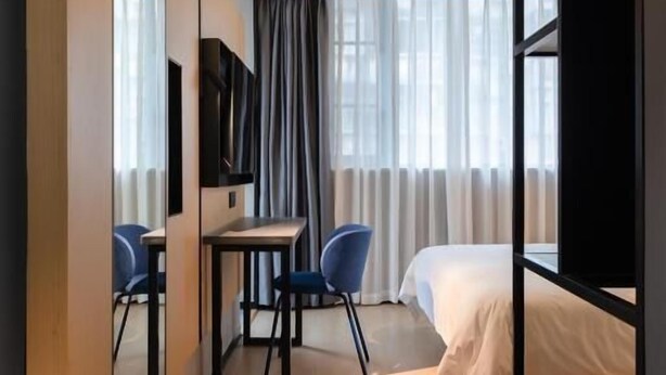 A modern hotel room with a bed, a desk with a chair, a TV, and a large mirror.