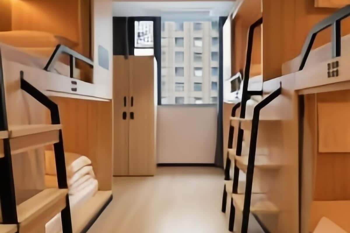 Een moderne hotelkamer met stapelbedden, een garderobe en uitzicht op een hoog gebouw.