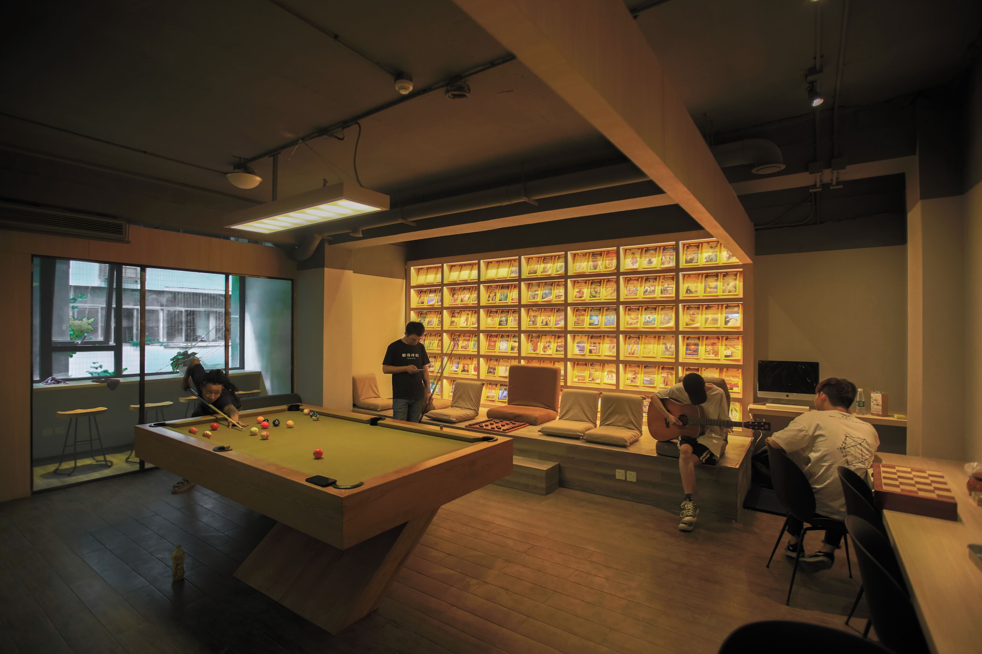 Un espace de loisirs intérieur moderne, doté d’une table de billard, de sièges et d’un mur recouvert de boîtes à en-cas illuminées.