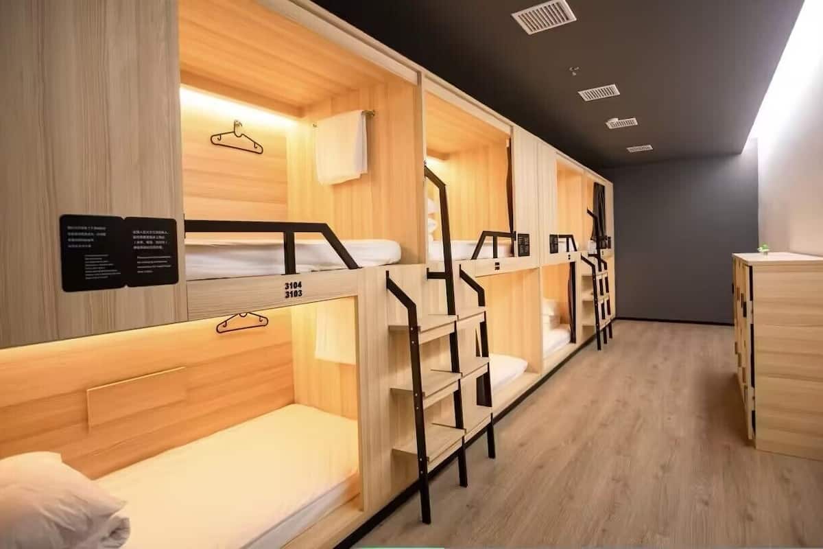 A dormitory room with bunk beds, wooden walls, and a blackboard with text.
