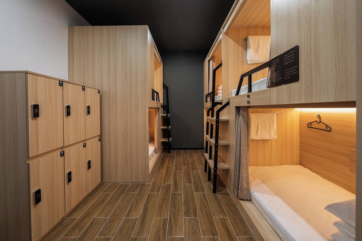 Une chambre d’hôtel compacte, dotée de casiers en bois, d’un lit superposé et d’un petit espace bureau.