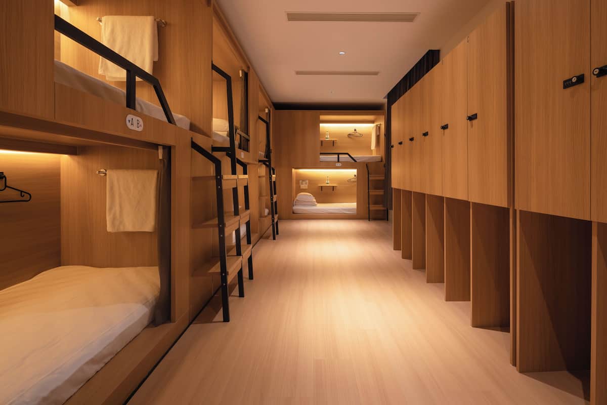 A bunk room with wooden bunk beds, a central walkway, and a small seating area with a bench and table.