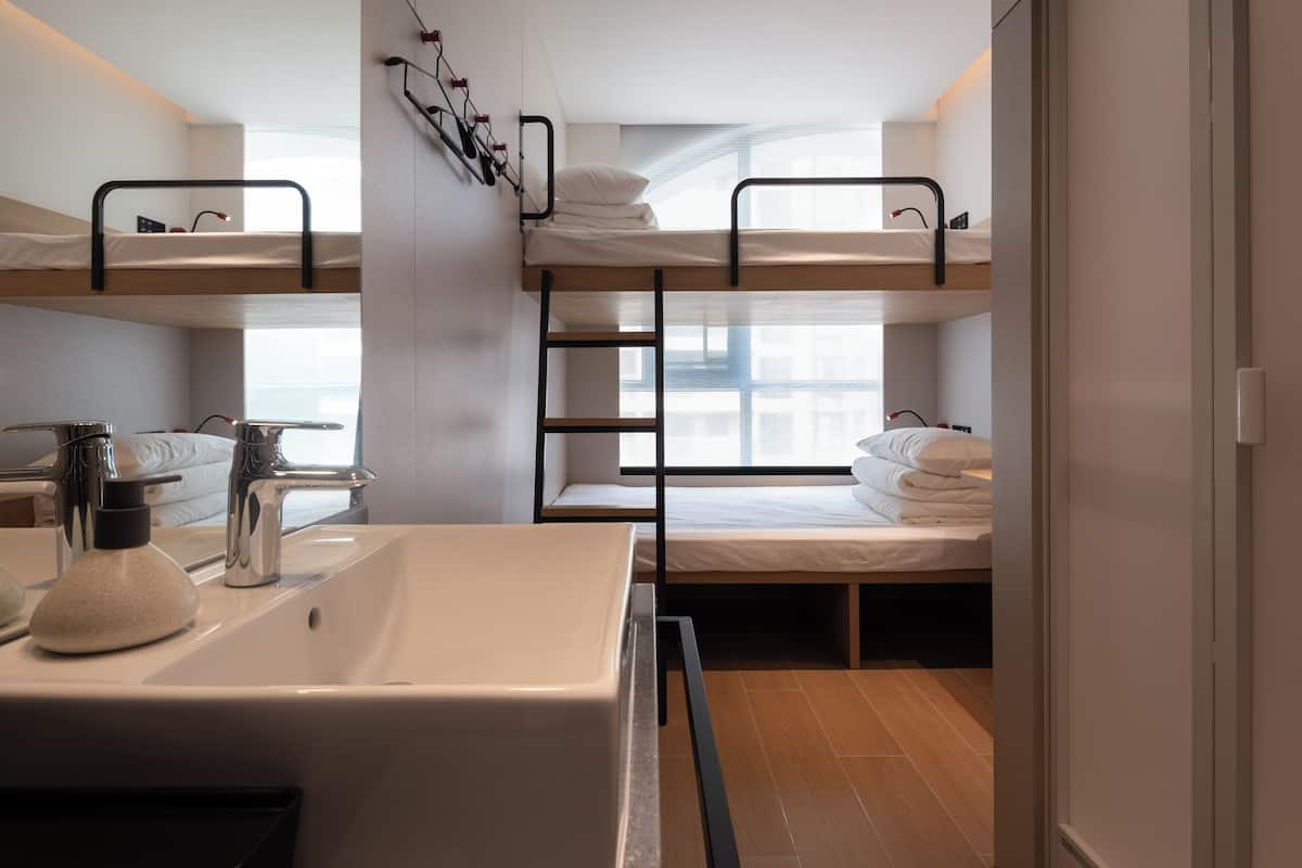 A modern hotel room with bunk beds, a large bathroom sink, and a window providing natural light.