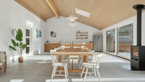 Eine geräumige Küche mit einem langen Holztisch und weißen Stühlen, einem eingebauten Herd und großen Fenstern.