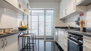 Eine moderne Küche mit weißen Schränken, einer schwarzen Arbeitsplatte und einem großen Fenster mit Jalousien.