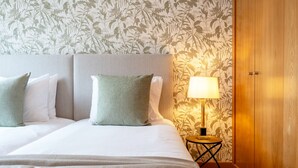 Ein ordentlich bezogenes Bett mit zwei Kissen, ein Nachttisch mit Lampe und ein Holzschrank.