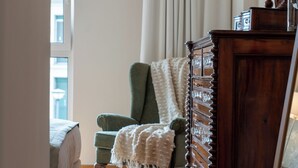 Ein Zimmer mit einem grünen Sessel, einer Holzkommode und einem Bett mit weißer Decke.