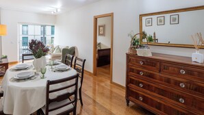 Ein Essbereich mit einem runden Tisch, gedeckt für vier Personen, Holzstühle, eine Kommode mit Schubladen und ein Spiegel an der Wand.