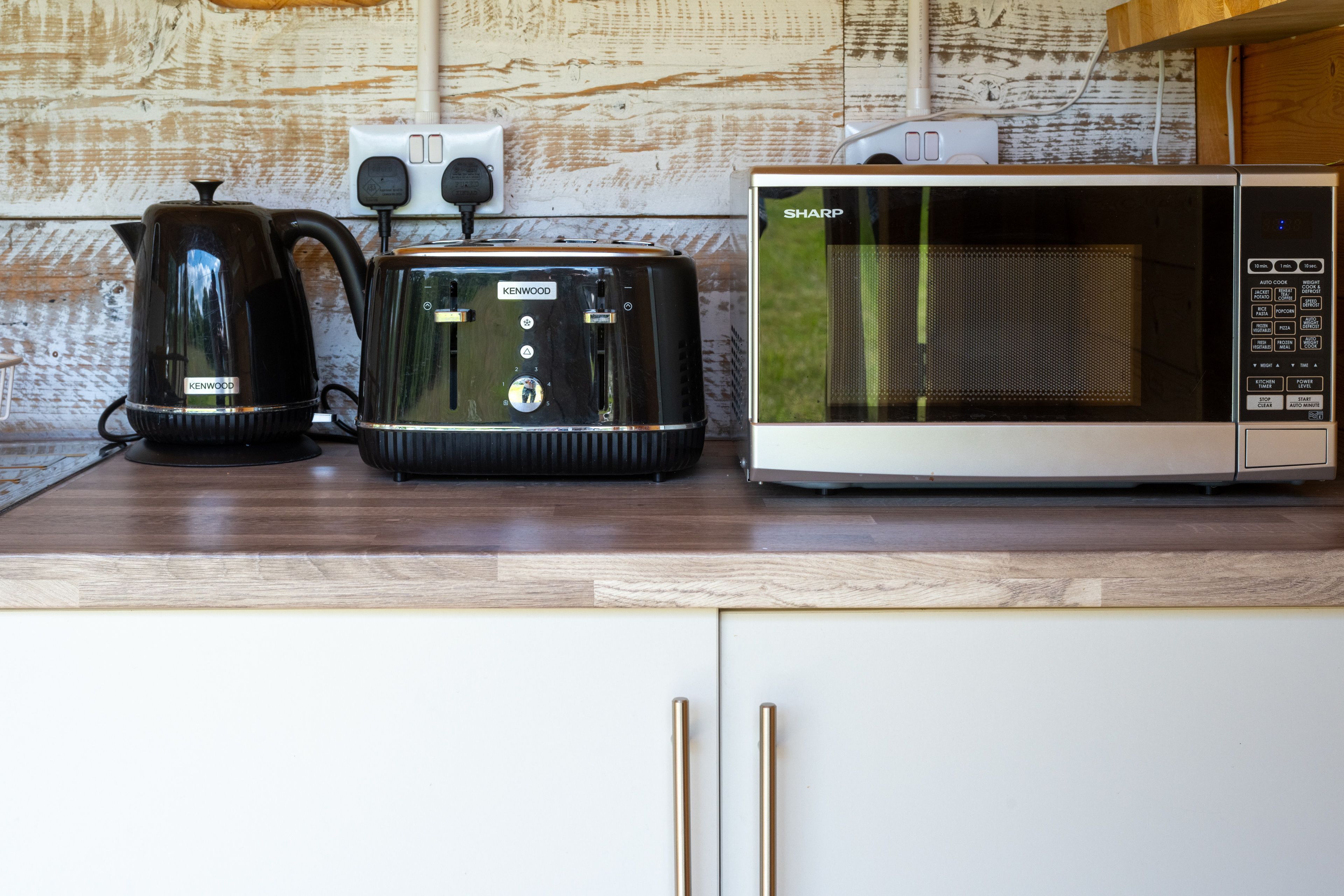 Una cocina con microondas, tostador Kenwood y hervidor sobre una encimera de madera.