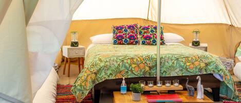 A tented room with a bed, a bedside table, and a colorful rug.