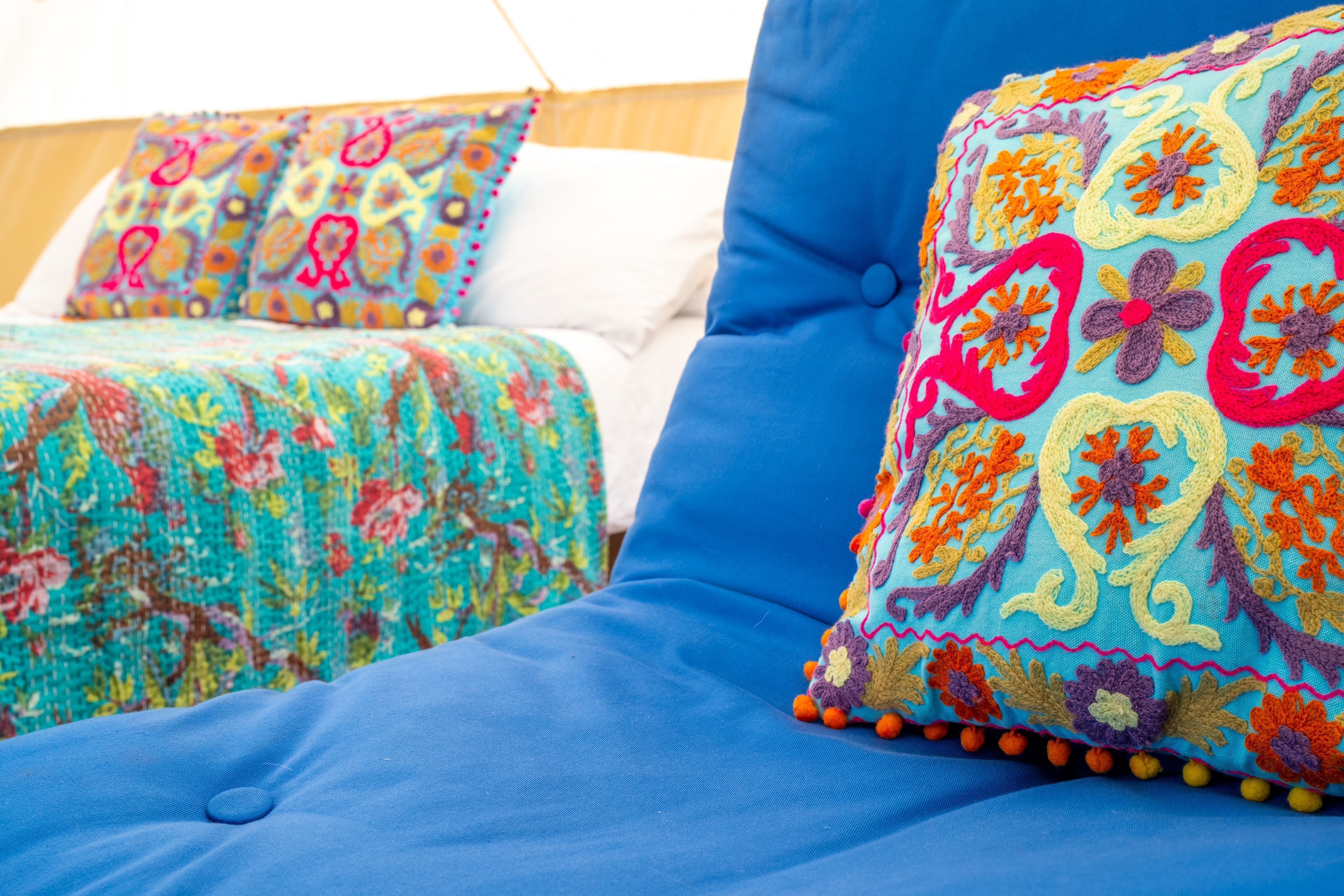 Ein Bett mit blauem, gepolsterten Kopfteil und farbenfrohen Stickkissen.