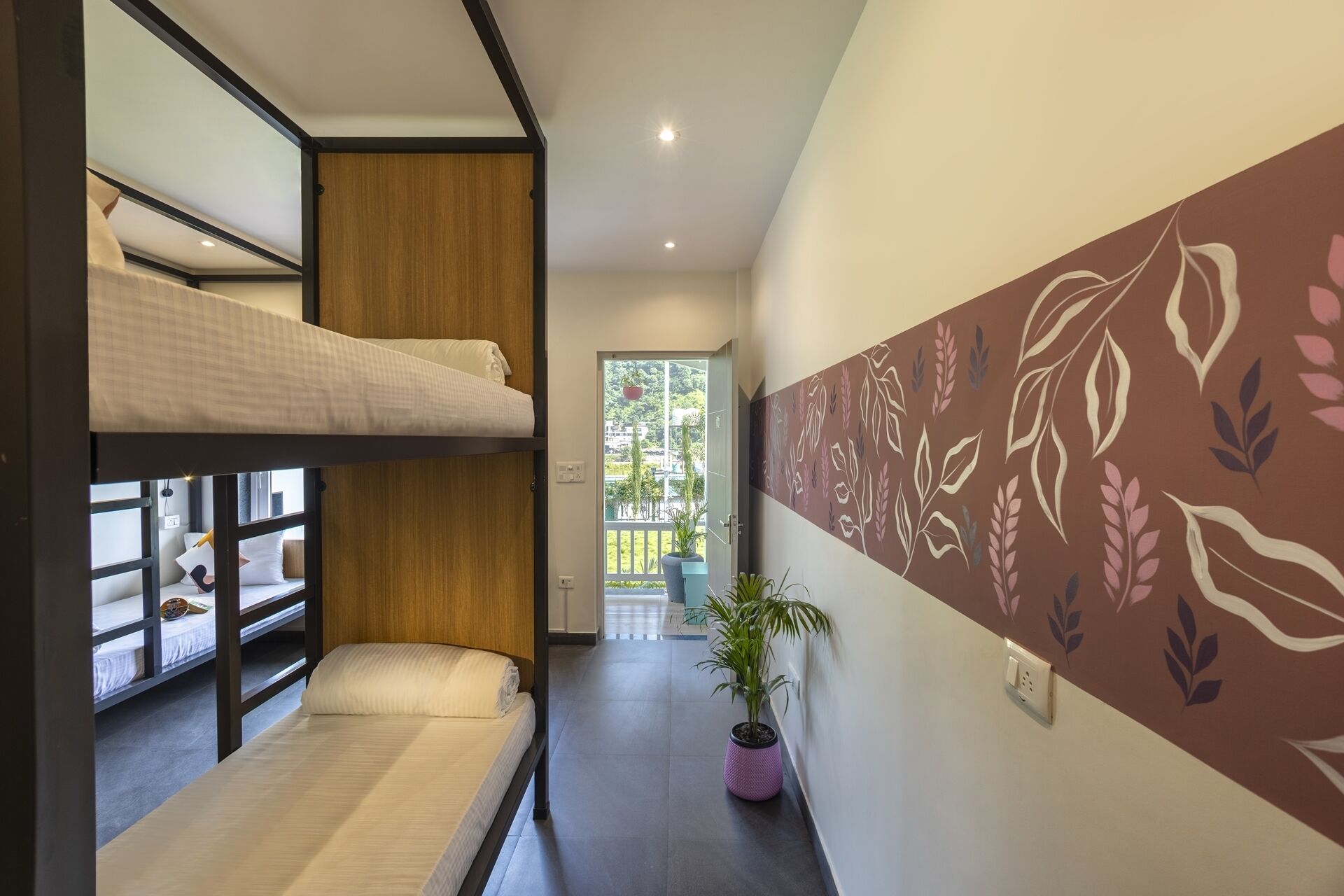A hotel room with bunk beds, a hallway with a plant, and a wall with a leaf pattern.