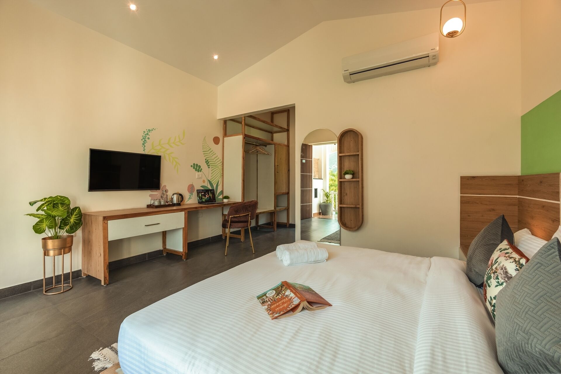 A modern hotel room with a bed, a desk, a TV, and a wardrobe.