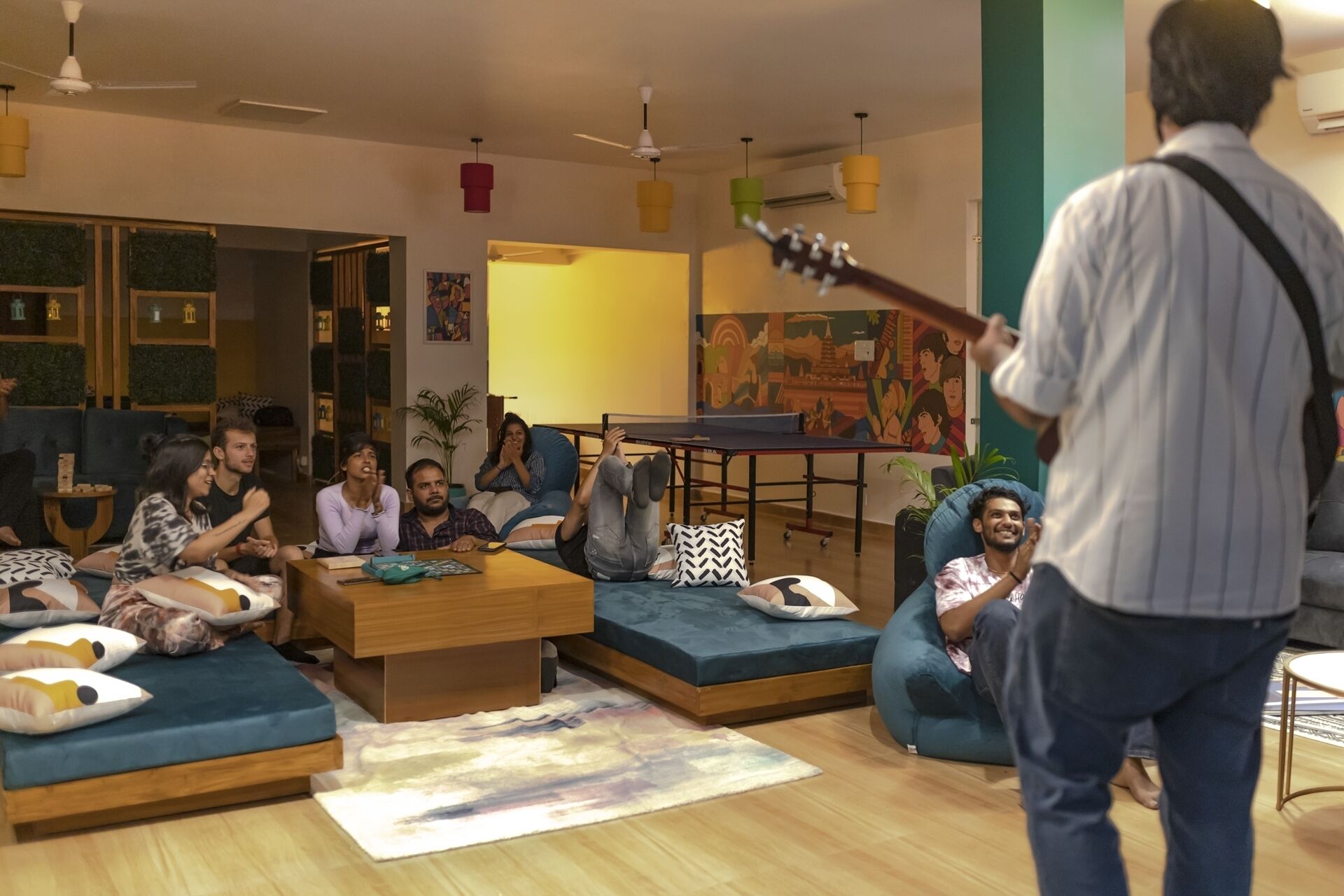 A modern living room with a ping pong table, sofas, and a person playing guitar.