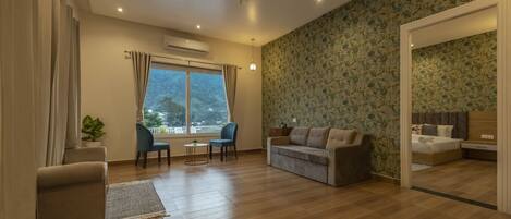 A spacious living room with a sofa, two armchairs, a coffee table, and a view of a mountainous landscape through large windows.