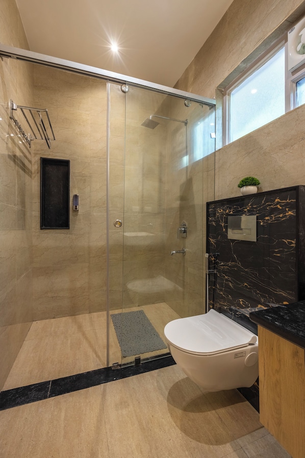 A modern bathroom with a glass-enclosed shower, a toilet, and a vanity with a marble countertop.