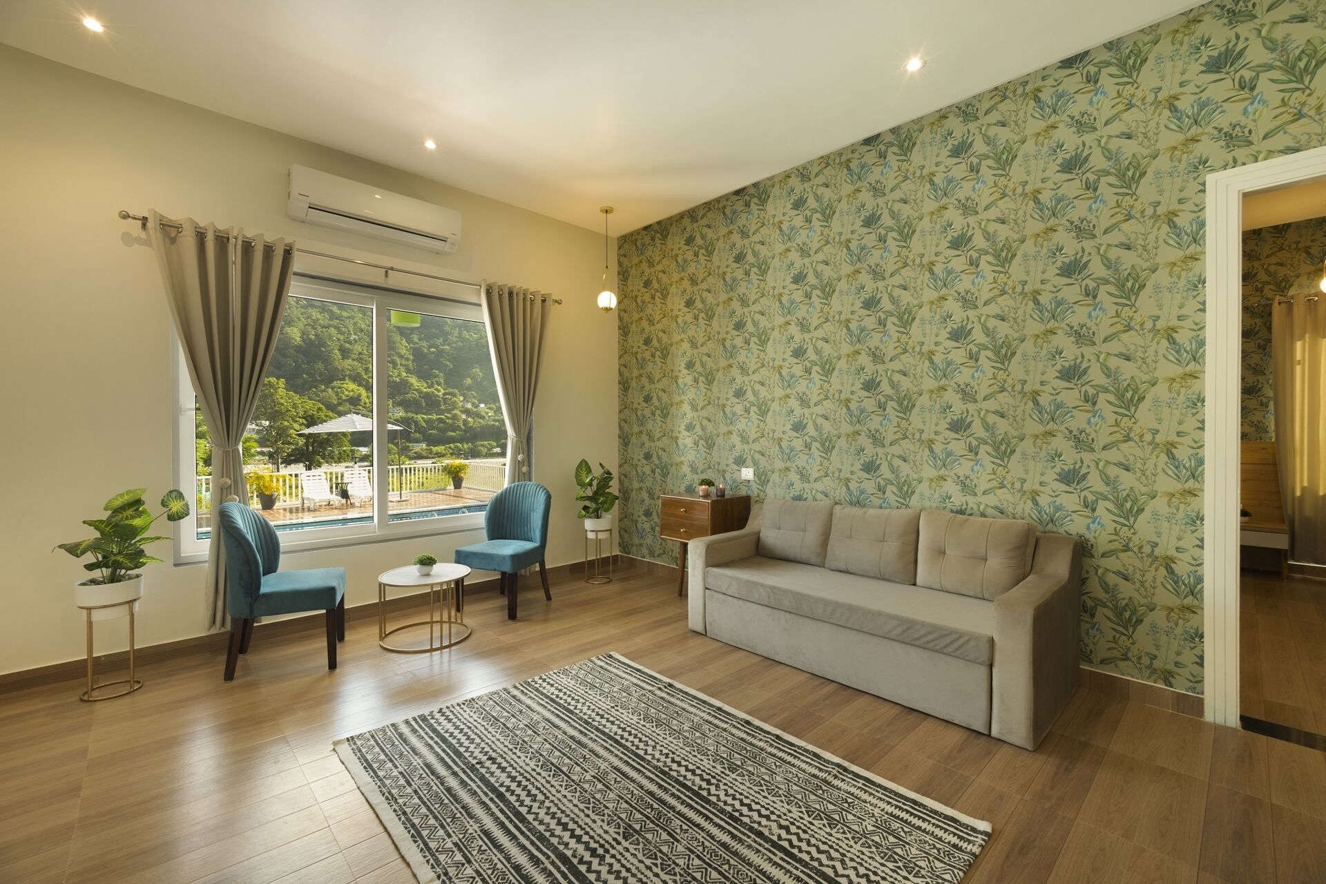 Een woonkamer met een bank, twee stoelen, een kamerkleed en uitzicht op een zwembad en groen buiten.