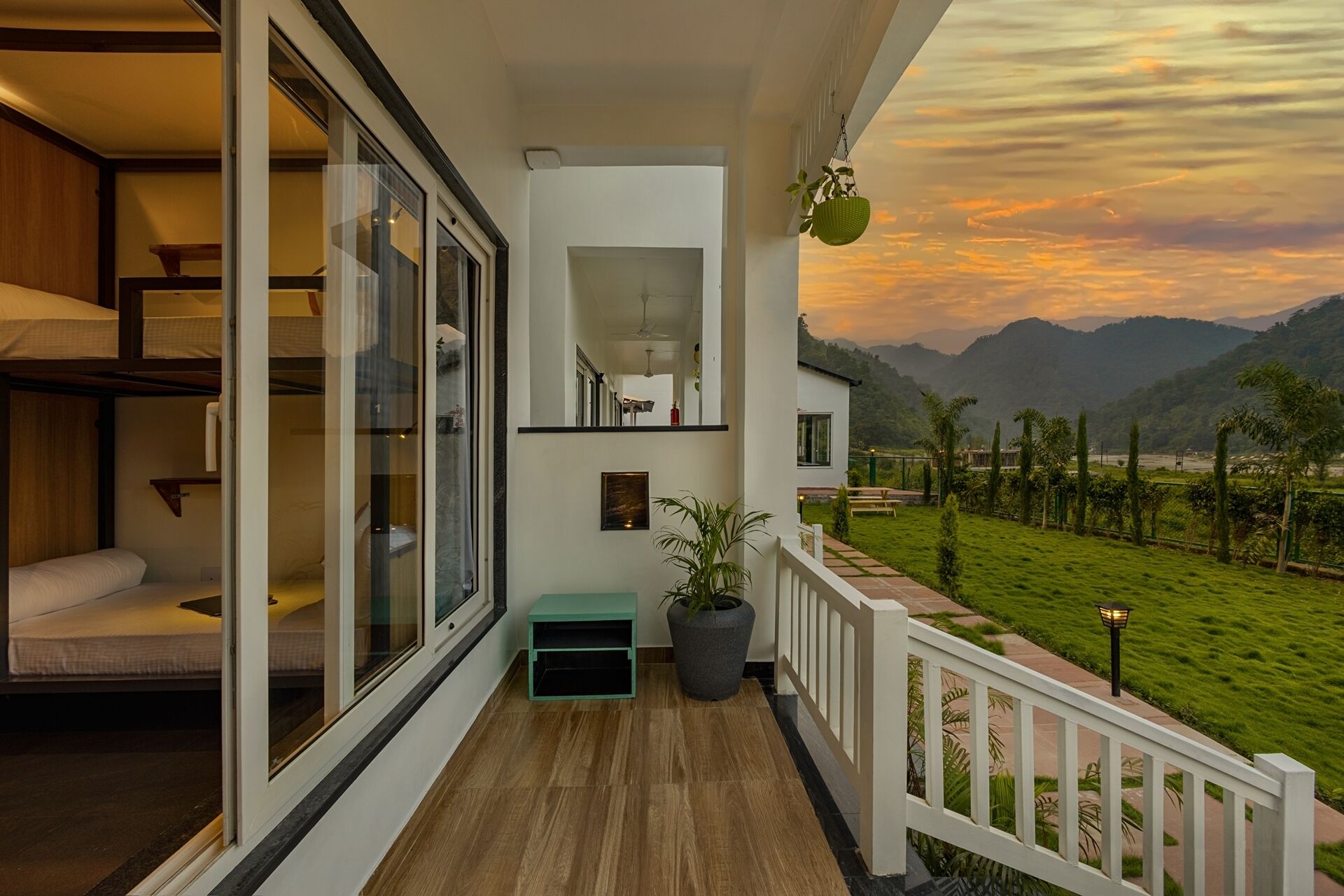 A balcony with a view of a sunset over mountains, a small seating area with a bench, and a potted plant.