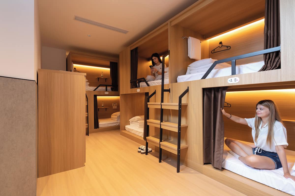 Een studentenkamer met stapelbedden, houten meubels en een kleine kast.