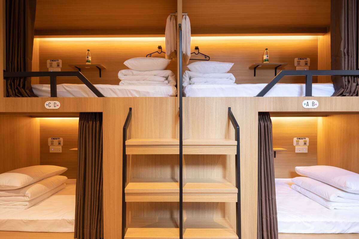 Een hotelkamer met twee bedden, houten wanden en een centraal geplaatst schap.