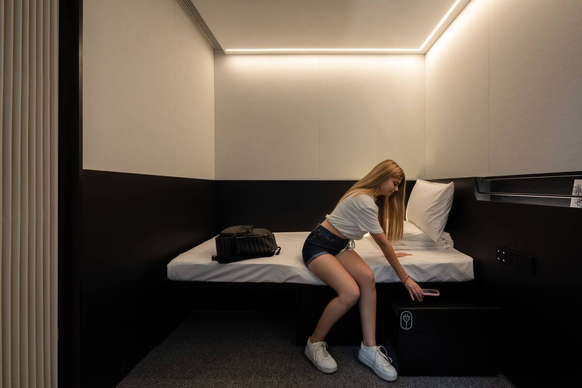Een enkel bed met een zwart hoofdeinde, een nachtkastje en een wandlamp.