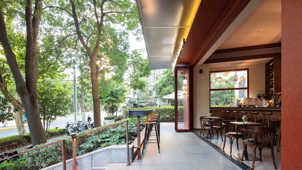 Un café moderne doté d’une terrasse, d’un escalier menant à un niveau inférieur et offrant une vue sur la rue et la verdure.