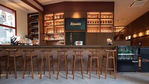Un espace bar avec des tabourets en bois, des étagères remplies de bouteilles d’alcool, un écran de télévision et un réfrigérateur.