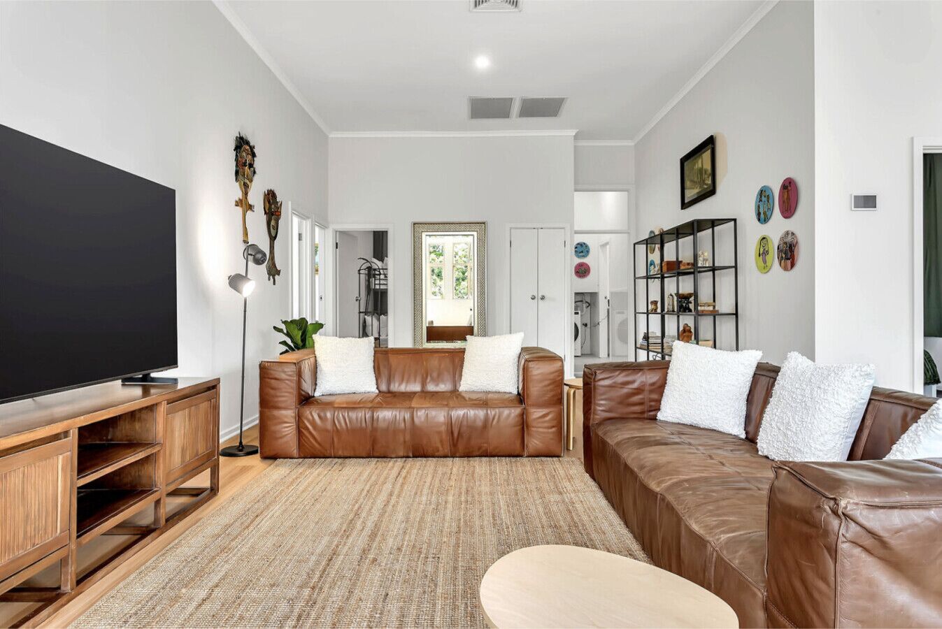 A modern living room with a brown leather sofa, a flat-screen TV, wooden entertainment unit, and a patterned rug.