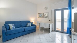 A living room with a blue sofa, a white desk, and a dining table. - GuestHost - Cozy 45 sqm apartment, able to accommodate up to 4 people, located on the sixth floor of a modern building with lift.The property is located in an extremely strategic area, just 100 meters from Santa Maria Novella station, near the historic c (Florence)
