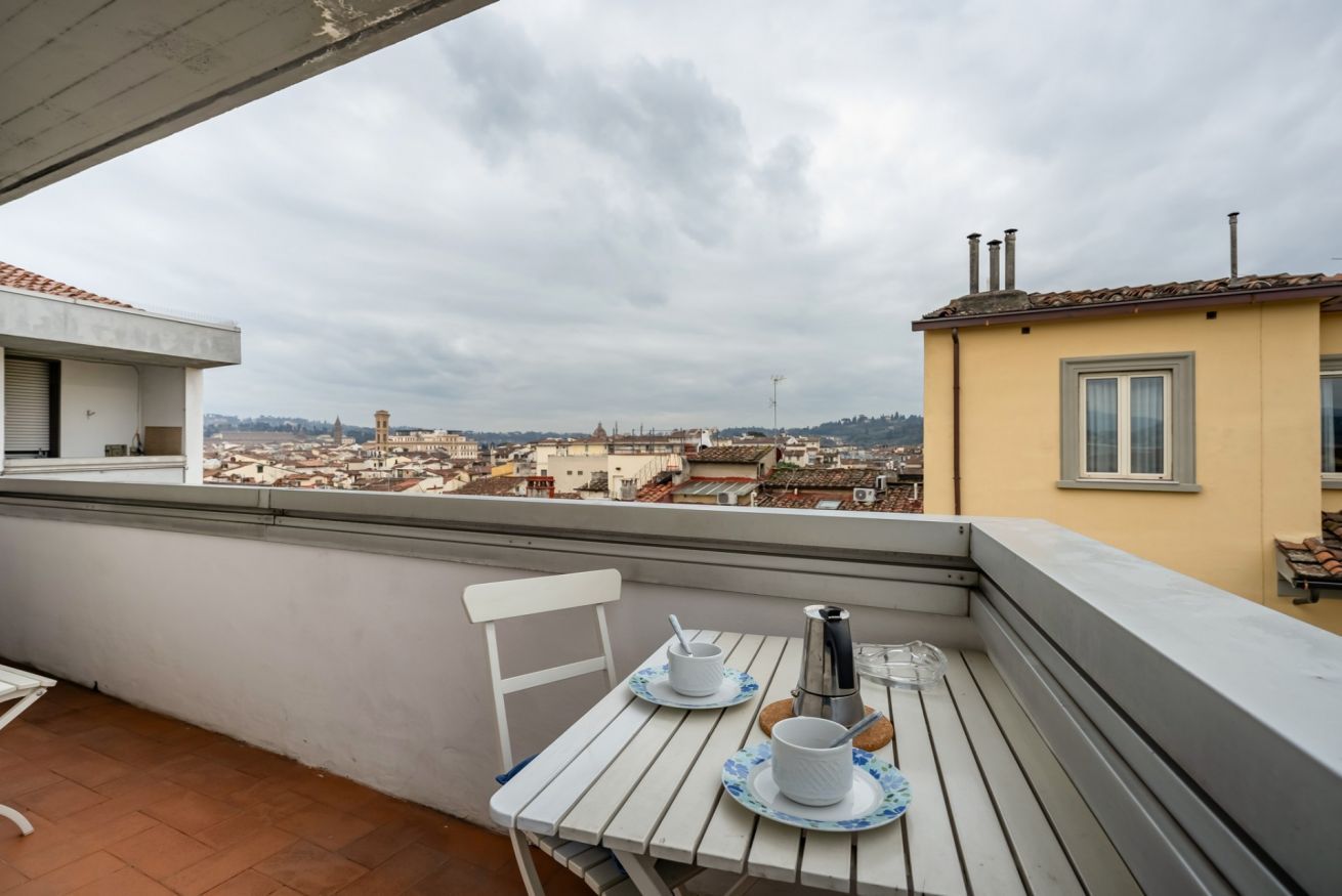 Un balcon avec une table dressée pour deux personnes, offrant une vue sur le paysage urbain.
