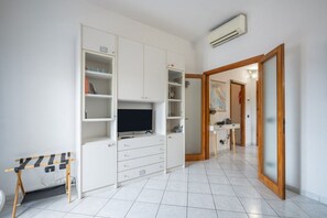 Quarto com guarda-roupa branco, televisão de tela plana, escrivaninha e banheiro visível por uma porta aberta.