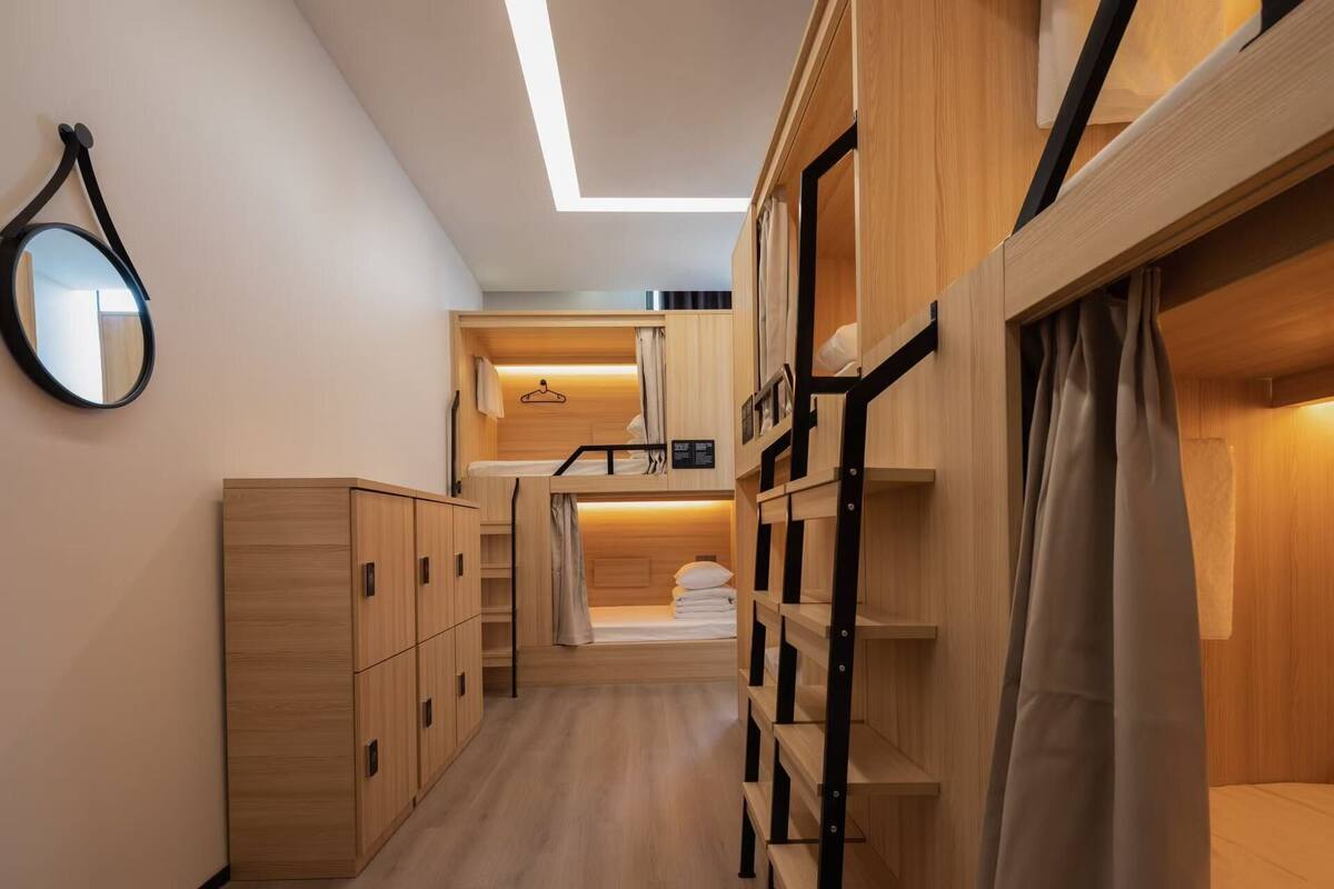 A compact hotel room with bunk beds, a wooden wardrobe, and a mirror on the wall.
