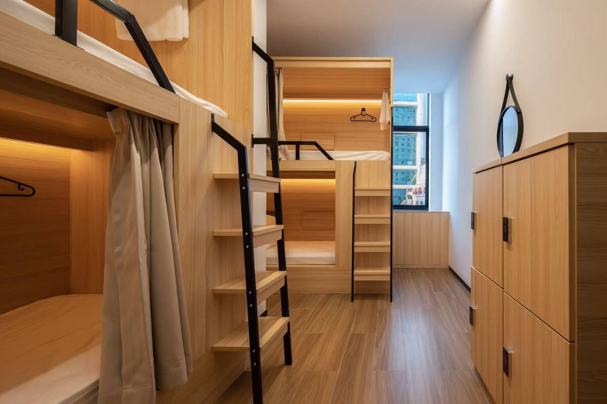 A compact, modern room with a bunk bed, wooden wardrobe, and a small window with a view.