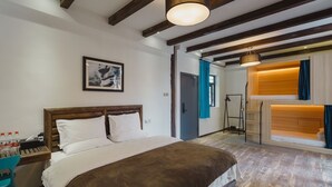 Una habitación de hotel con una cama grande, vigas de madera en el techo, un cuadro en la pared y un baño con ducha y lavamanos.