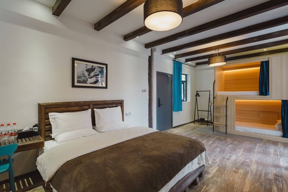 Ein Hotelzimmer mit einem großen Bett, Holzbalken an der Decke, einem gerahmten Bild an der Wand und einem Badezimmer mit Dusche und Waschbecken.
