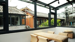 Habitación con vista a una arquitectura asiática tradicional a través de amplios ventanales, mobiliario de mimbre y una decoración interior moderna.