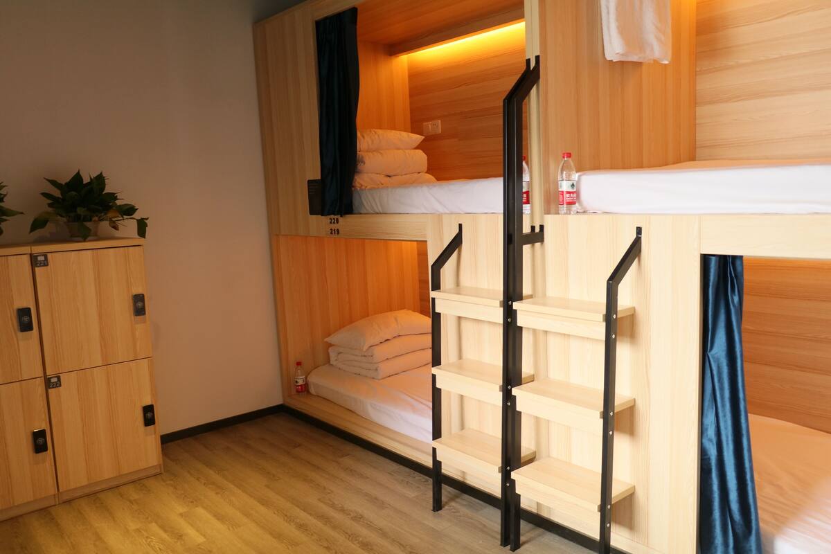 Ein Schlafraum mit Etagenbetten, Holzwänden und -böden, einem kleinen Regal und einem Blumentopf.