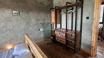 A room with a wooden bed, a wooden wardrobe with hanging space, and a concrete wall.