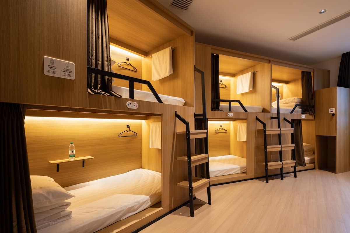Quarto de hotel pequeno com beliches, paredes de madeira e um nicho com uma garrafa.